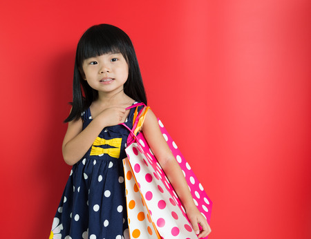 Little Asian girl holding shopping bags on red backgroundの写真素材
