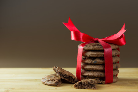 Stack of chocolate chips cookies tied up with red ribbon on chop boardの写真素材