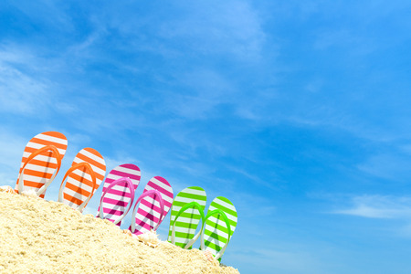Row of multicolor flip flops on beach against blue skyの写真素材