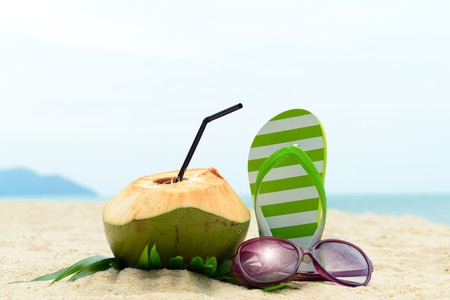 Pair of green striped sandal, sunglasses and coconut on the beachの写真素材