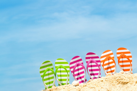 Row of multicolor flip flops on beach against blue skyの写真素材