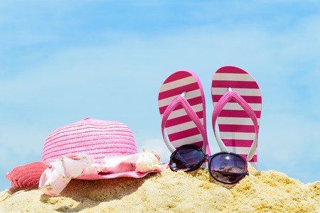 Pink flip flop, sunglasses and floppy hat at the beachの写真素材