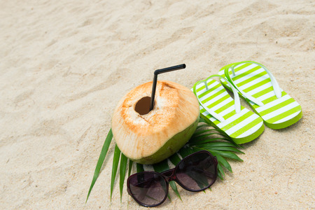 Pair of green striped sandal, sunglasses and coconut on the beachの写真素材