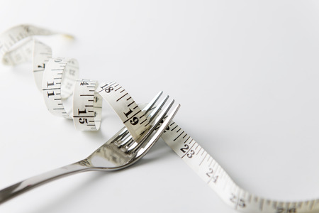 Diet concept illustrated with fork and measuring tape over white backgroundの写真素材