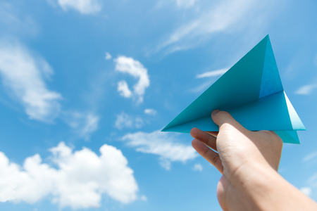 Hand launching paper plane toward cloudy blue skyの写真素材
