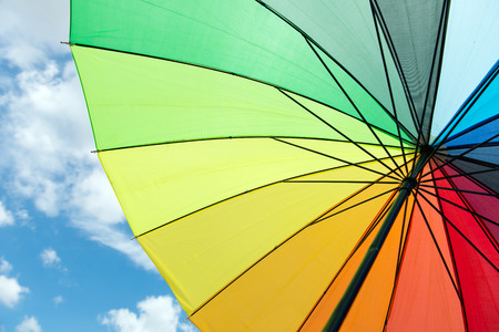 Close up of rainbow umbrella against cloudy blue skyの写真素材