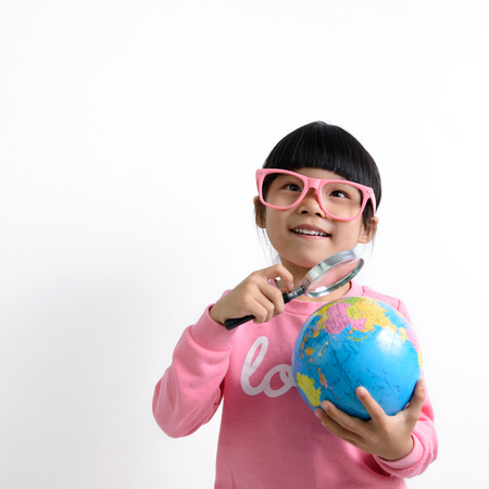 Little Asian girl holding magnifying glass on earth globe