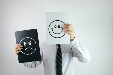 Businessman holding two papers with happy and angry face each on them Businessman holding two papers with happy and angry face each on them