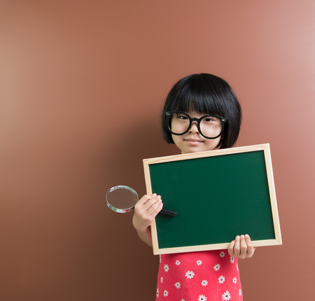 Asian school child hold a blank chalkboard and a magnifying glass for education conceptualの写真素材