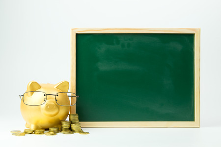 Golden color piggy bank with stacks of gold coins beside blank chalkboardの写真素材