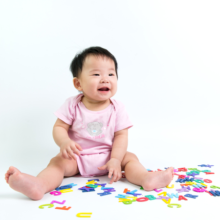 Asian baby playing wooden alphabets happily on white backgroundの写真素材