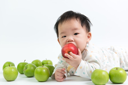 Asian baby eating red apple on white backgroundの写真素材