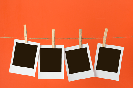Blank photos hanging on rope over orange backgroundの写真素材