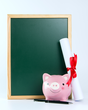Piggy bank and certificate standing next to blank blackboard, with copy spaceの写真素材