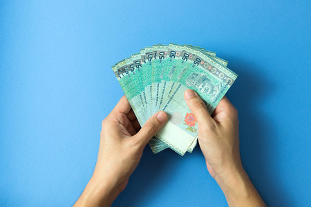 Hand with fifty Ringgit Malaysia currency notes over blue background