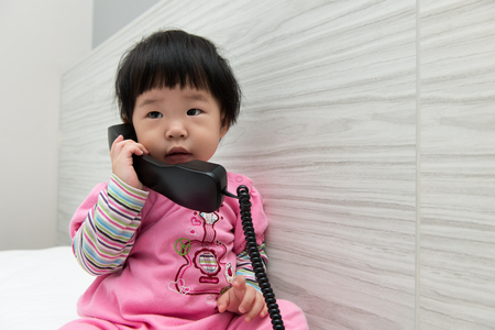 Asian toddler sitting on bed speaking to the phoneの写真素材
