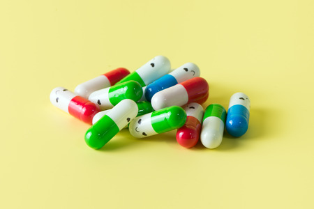 Pile of supplement capsules or drugs with smiling face over yellow background