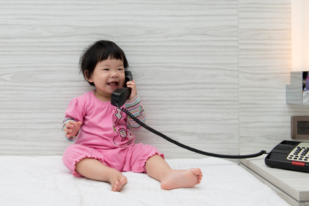Asian toddler sitting on bed speaking to the phoneの写真素材