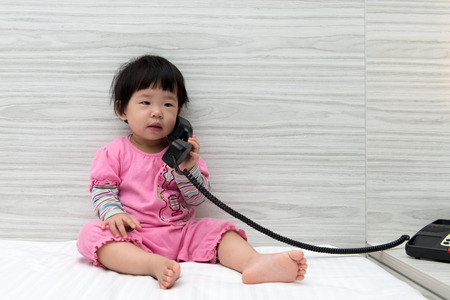Asian toddler sitting on bed speaking to the phoneの写真素材
