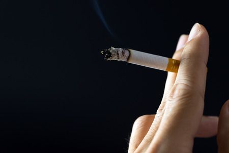 Close up of hand holding cigarette over black backgroundの写真素材