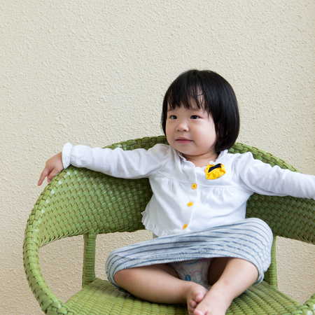 Asian toddler girl sitting on chair smilingの写真素材