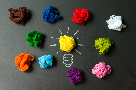 Great idea concept with light bulb among multicolor yarn balls over black backgroundの写真素材