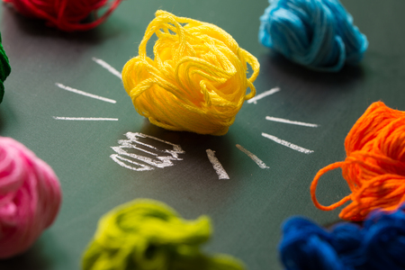 Great idea concept with light bulb among multicolor yarn balls over black background