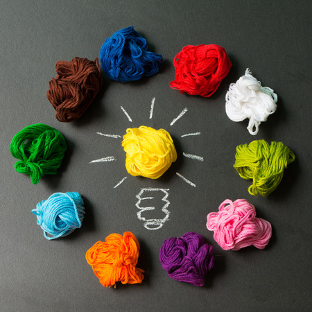 Great idea concept with light bulb among multicolor yarn balls over black backgroundの写真素材