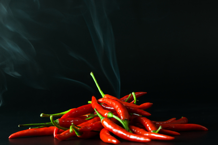 Pile of red hot chilli pepper with smoke going up over black backgroundの写真素材