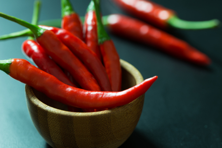 Red chili peppers on wooden bowl over black backgroundの写真素材