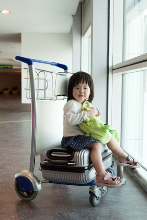 Little Asian baby sitting on luggage with trolley at airportの写真素材