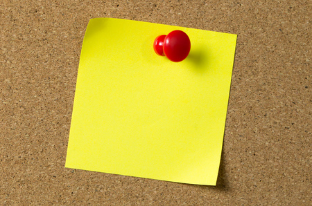 Blank yellow sticky note pad pinned to corkboard using a red thumb tack pinの写真素材