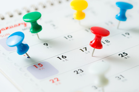 Various color thumb tack pins on calendar as reminderの写真素材