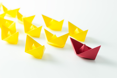 Leadership concept with a red paper ship leading among yelllow shipsの写真素材