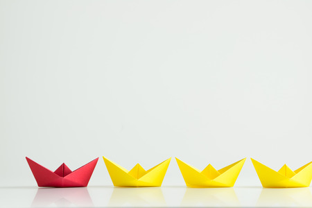 Leadership concept with a red paper ship leading among yelllow ships in a rowの写真素材