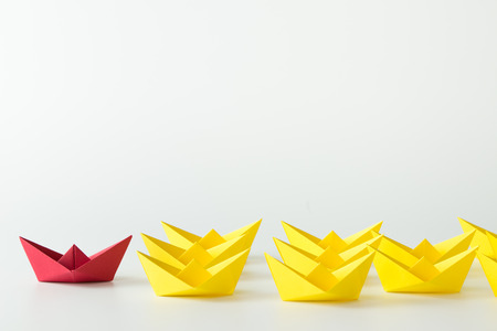 Leadership concept with a red paper ship leading among yelllow shipsの写真素材