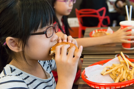 Little Asian girl eating a hamburger and french fries in the restaurantの写真素材