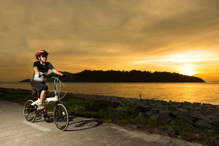 Silhouette of a senior woman cyclist at sunset or sunrise near oceanの写真素材