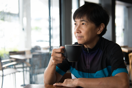Portrait of a senior Asian woman in cycling jersey hold a cup of coffeeの写真素材