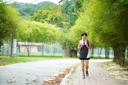Front view of senior Asian woman jogging through parkの写真素材