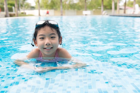 Portrait of Asian teen girl with goggles playing in swimming poolの写真素材