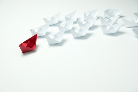 Leadership concept with a red paper ship leading among white ships on blue backgroundの写真素材