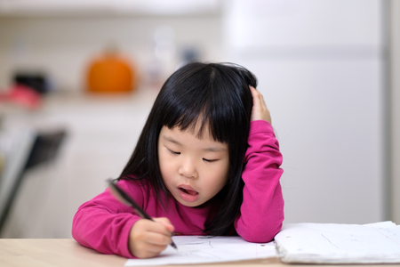 Young little Asian girl learning to write on piece of paperの写真素材