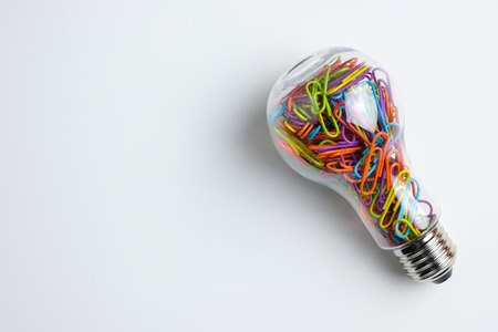 Light bulb filled with multicolor paper clips isolated on white backgroundの写真素材