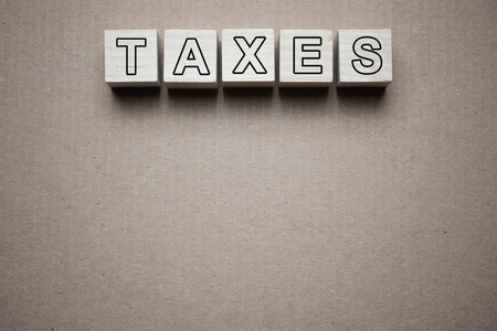 Taxes text written on wooden blocks isolated on piece of grey paperの写真素材