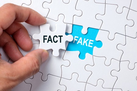 Fake word on missing puzzle with a hand hold a piece of fact word puzzle