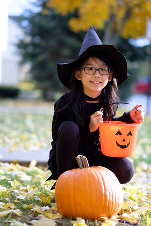 Portrait of little asian girl in witch costume with pumpkin for halloween celebrationの写真素材