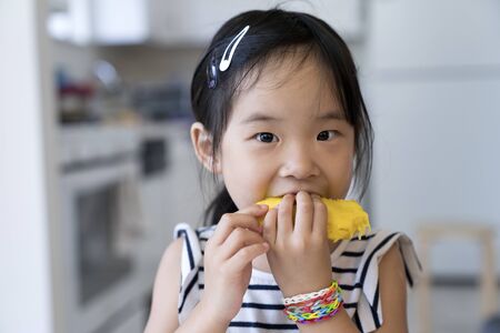Happy cute little Asian girl eating mango with funny face