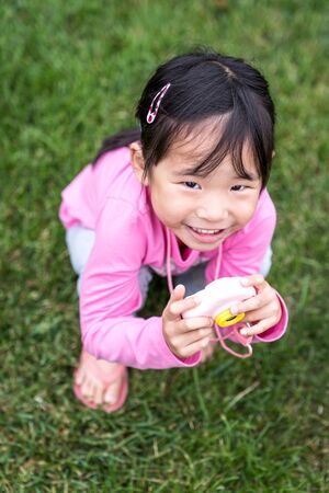Portrait of an asian little girl holding a plastic camera toy at outdoorの写真素材