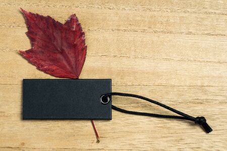 Blank black label tag with leaves on wooden background for autumn or fall designの写真素材